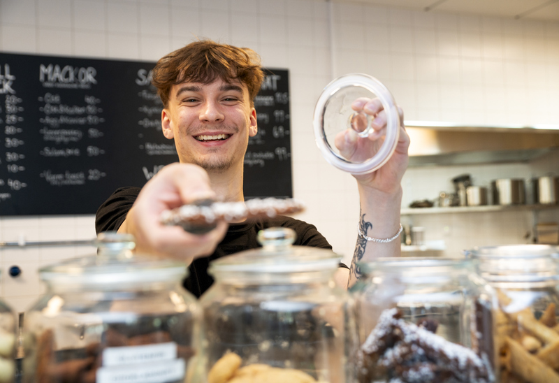 En persom som arbetar på ett café håller i en kaka. 