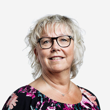 Porträttbild på kvinna med blont, kort vågigt hår. Hon bär glasögon, småler och bär en blommig tröja med svart bas.