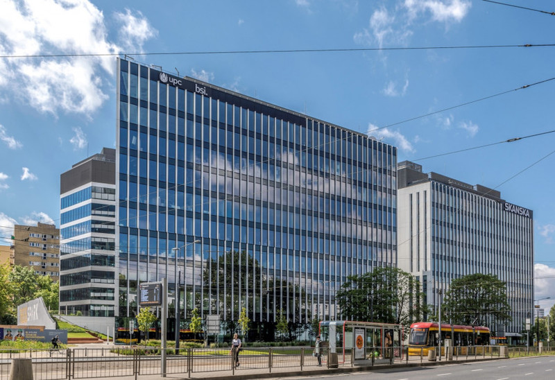 Modern husfasad i glas, nära finns en busstation och himlen är blå