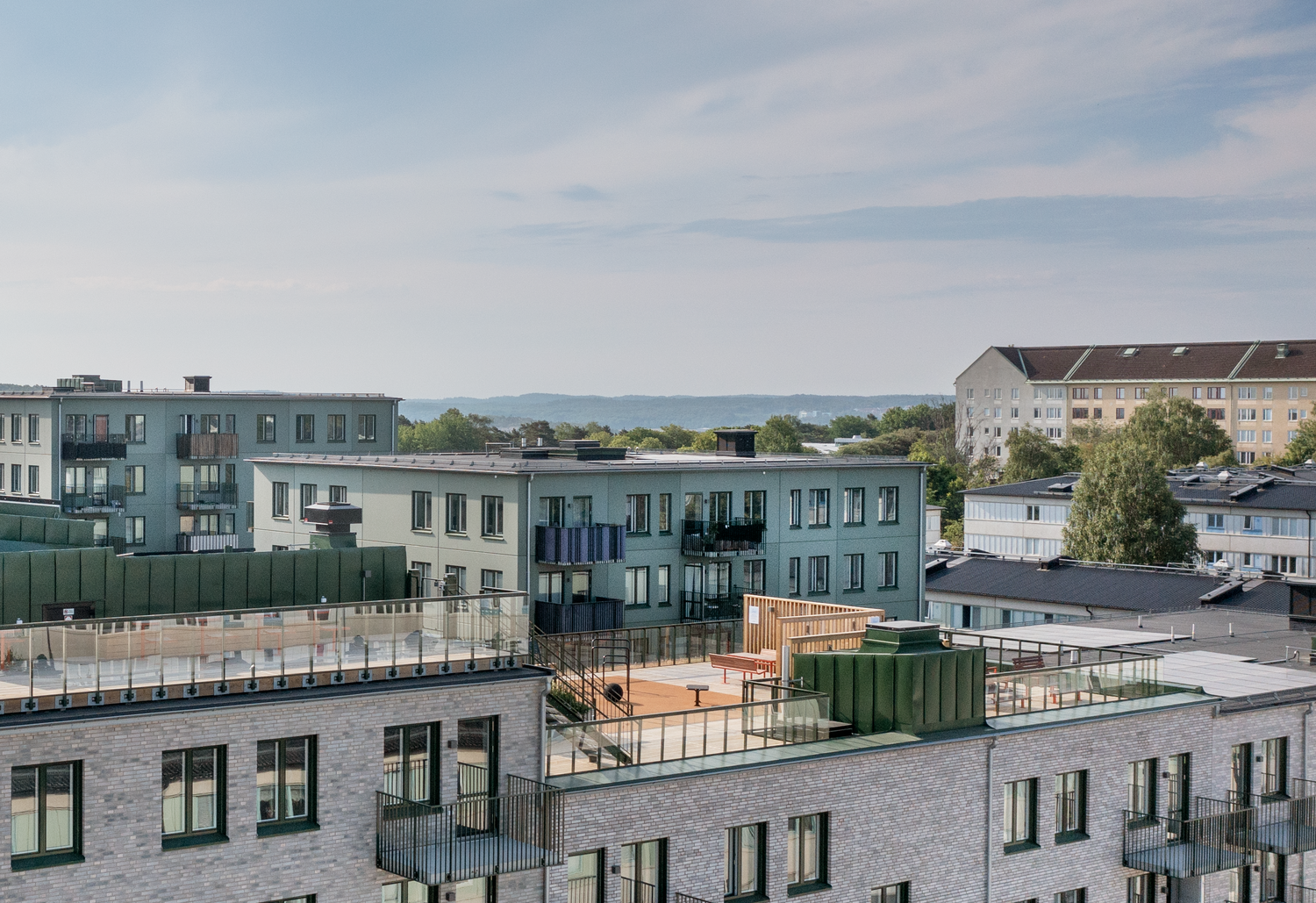 Byggnader och takpark i Ekebäckshöjd, i Göteborg en solig dag med skira moln på himlen. Det är stora terrasser med mycket grönska på. 