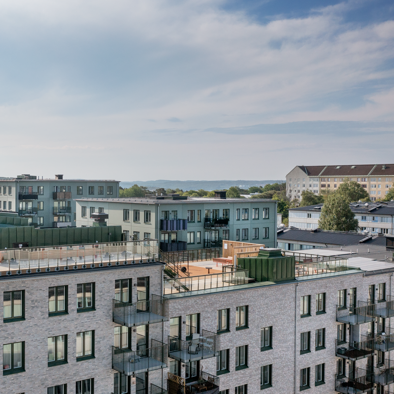 Byggnader och takpark i Ekebäckshöjd, i Göteborg en solig dag med skira moln på himlen. Det är stora terrasser med mycket grönska på. 