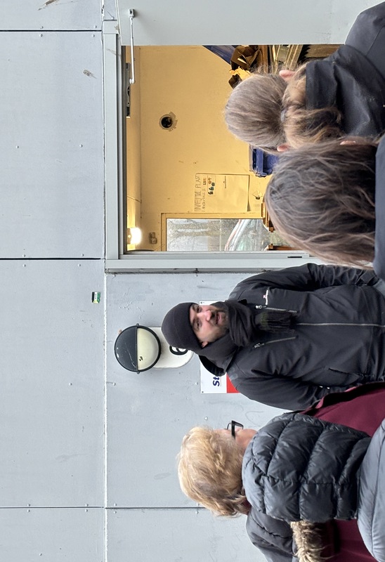 En mörklädd man står utanför ett soprum och pratar med andra människor