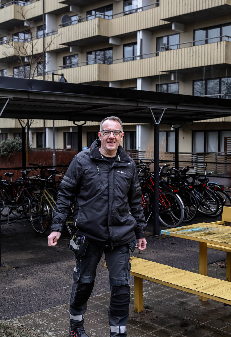 En person står framför ett cykelskjul med flera parkerade cyklar. I bakgrunden syns en flerfamiljsbyggnad med balkonger.