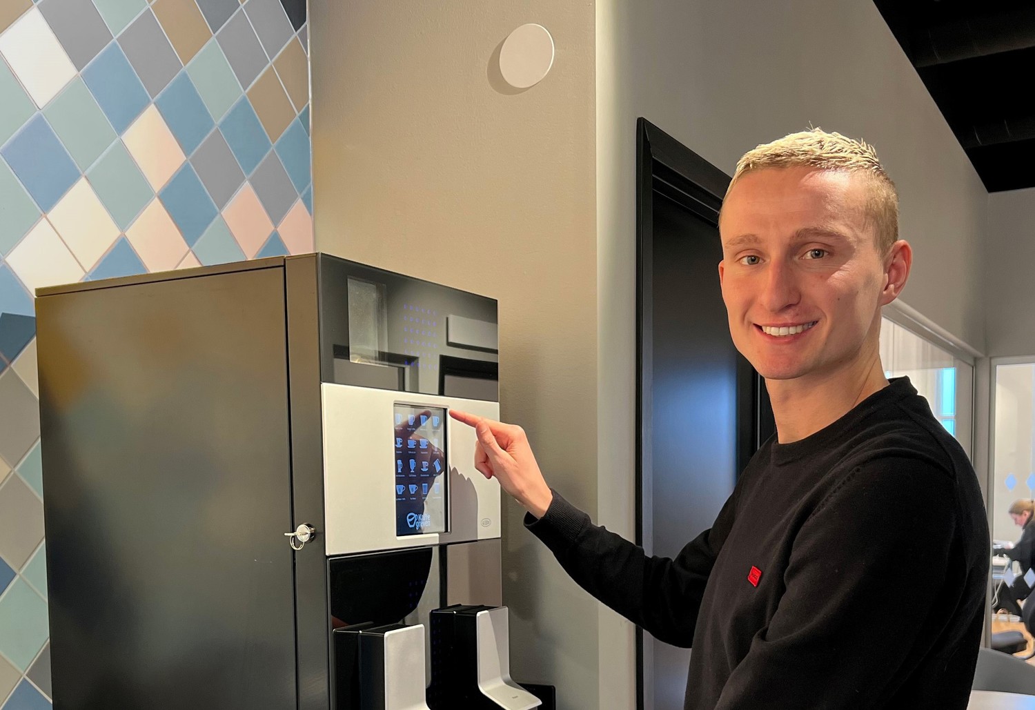 Leende kille trycker på knapparna på en kaffemaskin