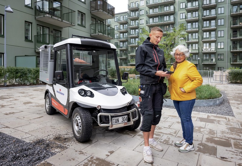 Fastighetsvärden Oliver samtalar med en kund i bostadsområde, i bakgrunden en grön fasad.