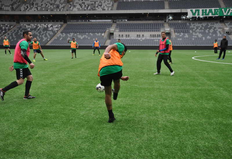 Flera fotbollsspelare på en inomhusarena med läktare i bakgrunden