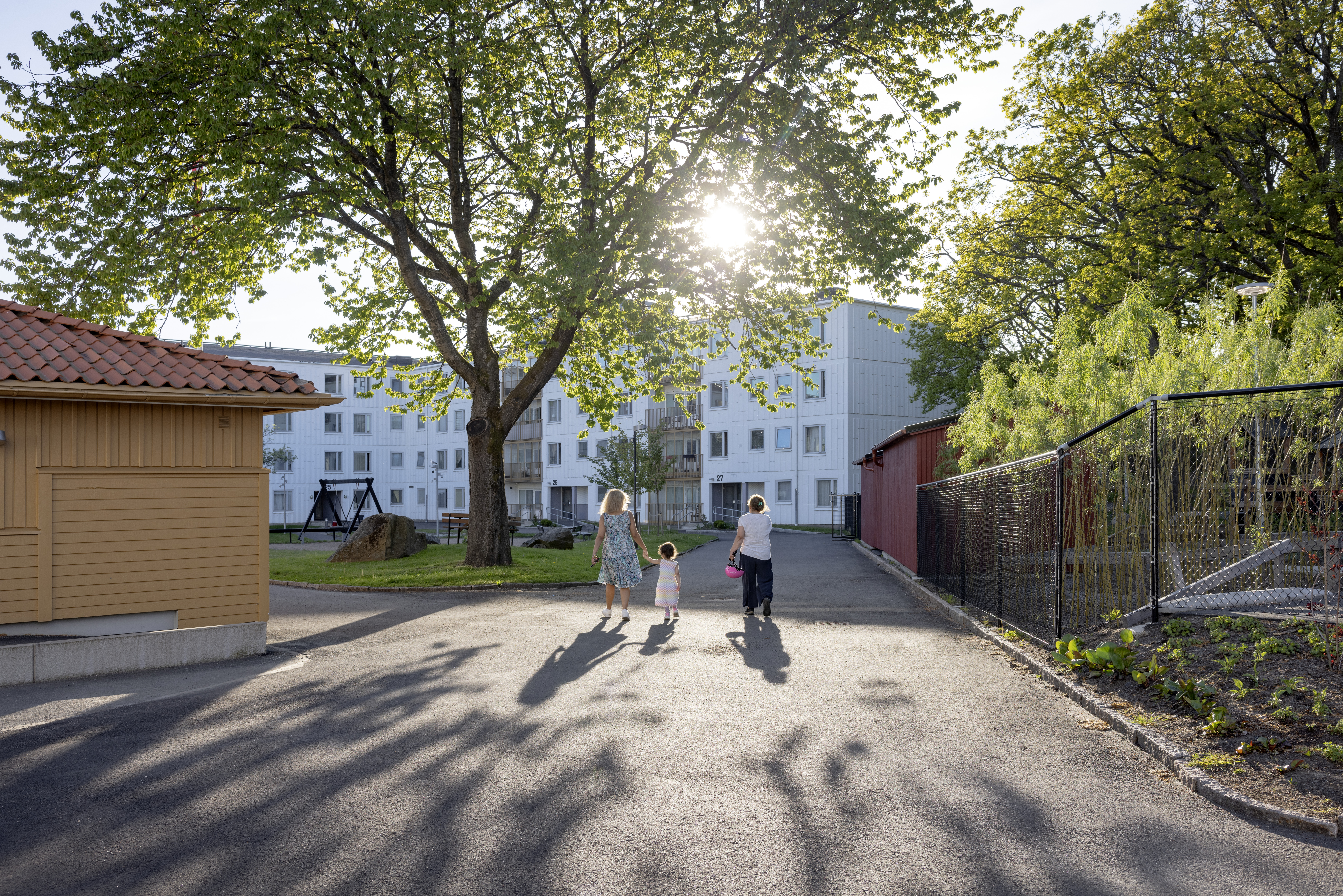 Bilden visar en familj som går i ett soligt bostadsområde, tillhörande Stena Fastigheter, i Tynnered i Göteborg