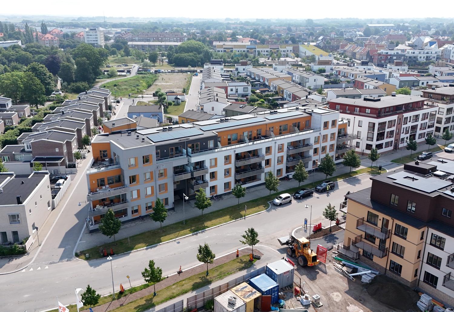 Flygbild över ett nybyggt bostadsområde med flerbostadshus, radhus, gator och grönska.