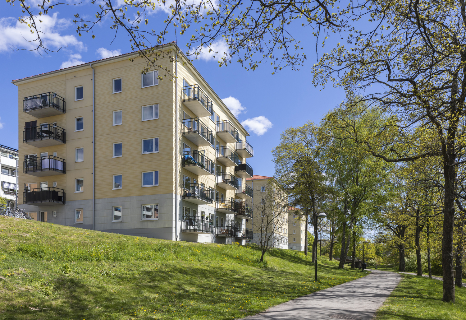 Ett ljusgult flerfamiljshus med ett träd i förgrunden.