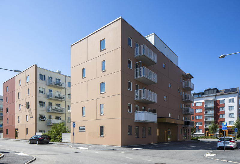 Flera moderna flerfamiljshus i olika färger vid en gatukorsning under en klarblå himmel