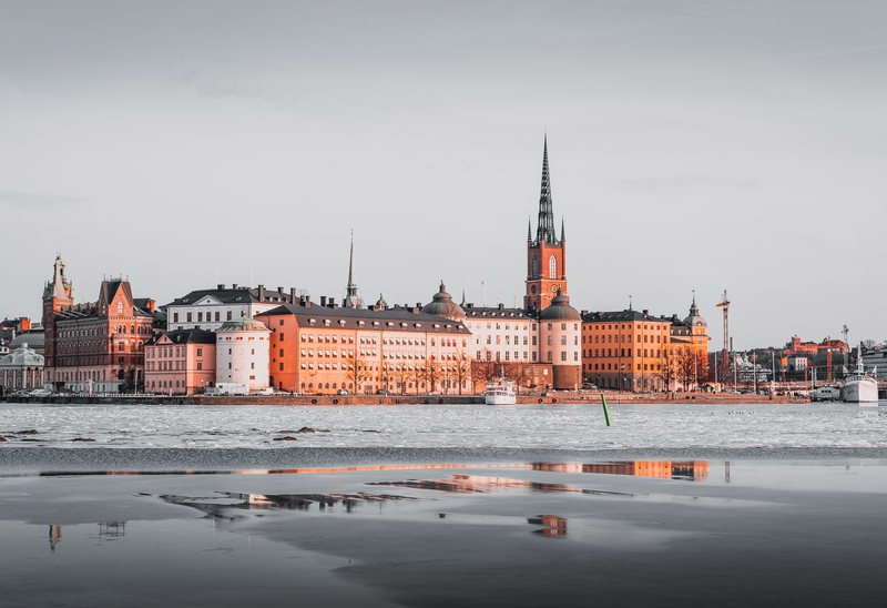 Vy över en stadssilhuett vid vattnet med historiska byggnader och en kyrkspira i centrum.