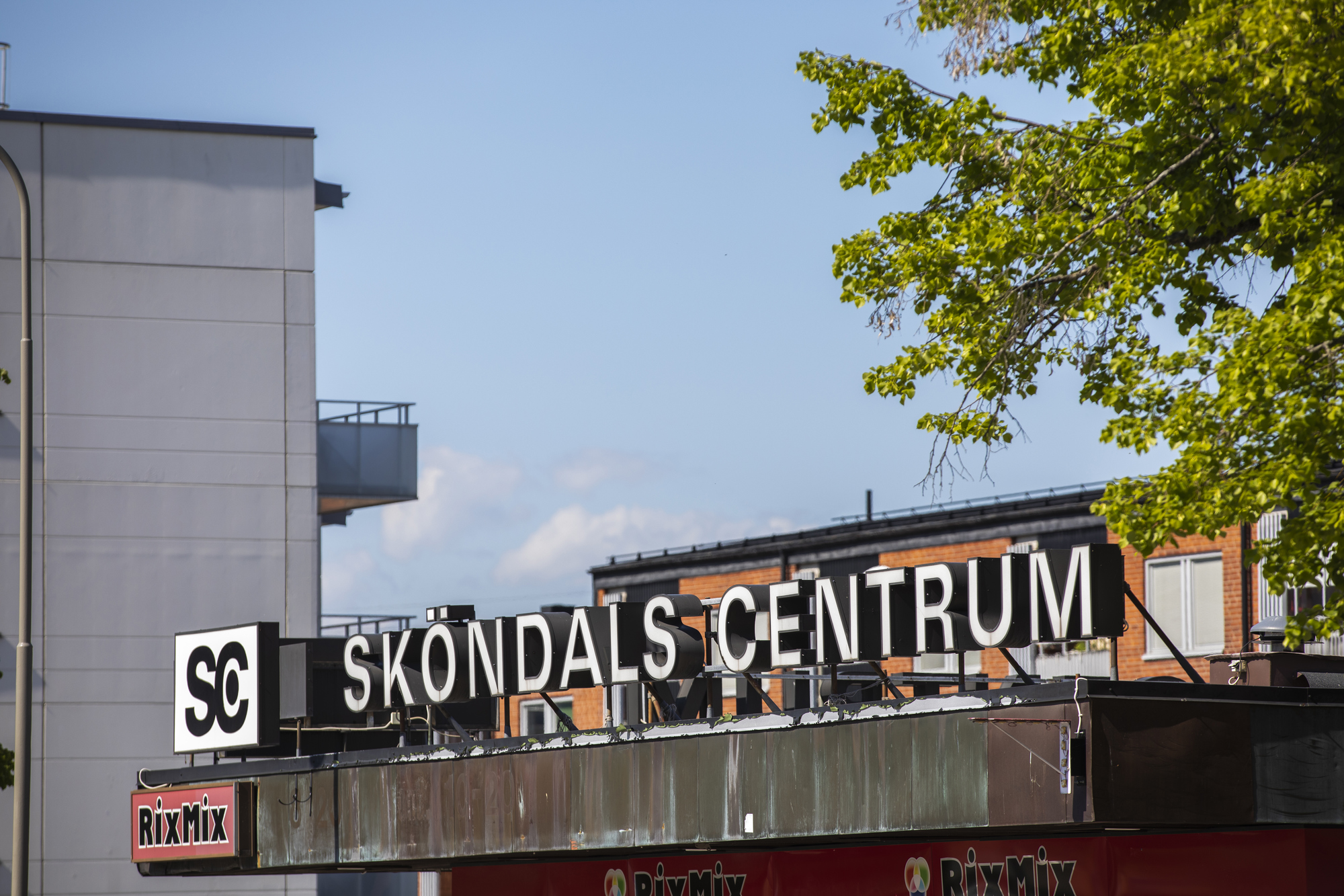 Sköndals centrums skylt på tak i fokus med hus i bakgrund