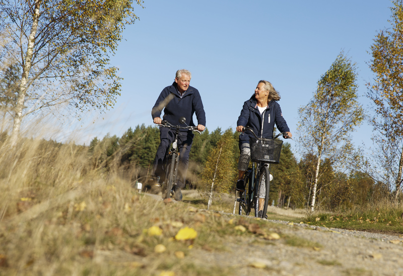 Två seniorer cyklar på en landsväg. 
