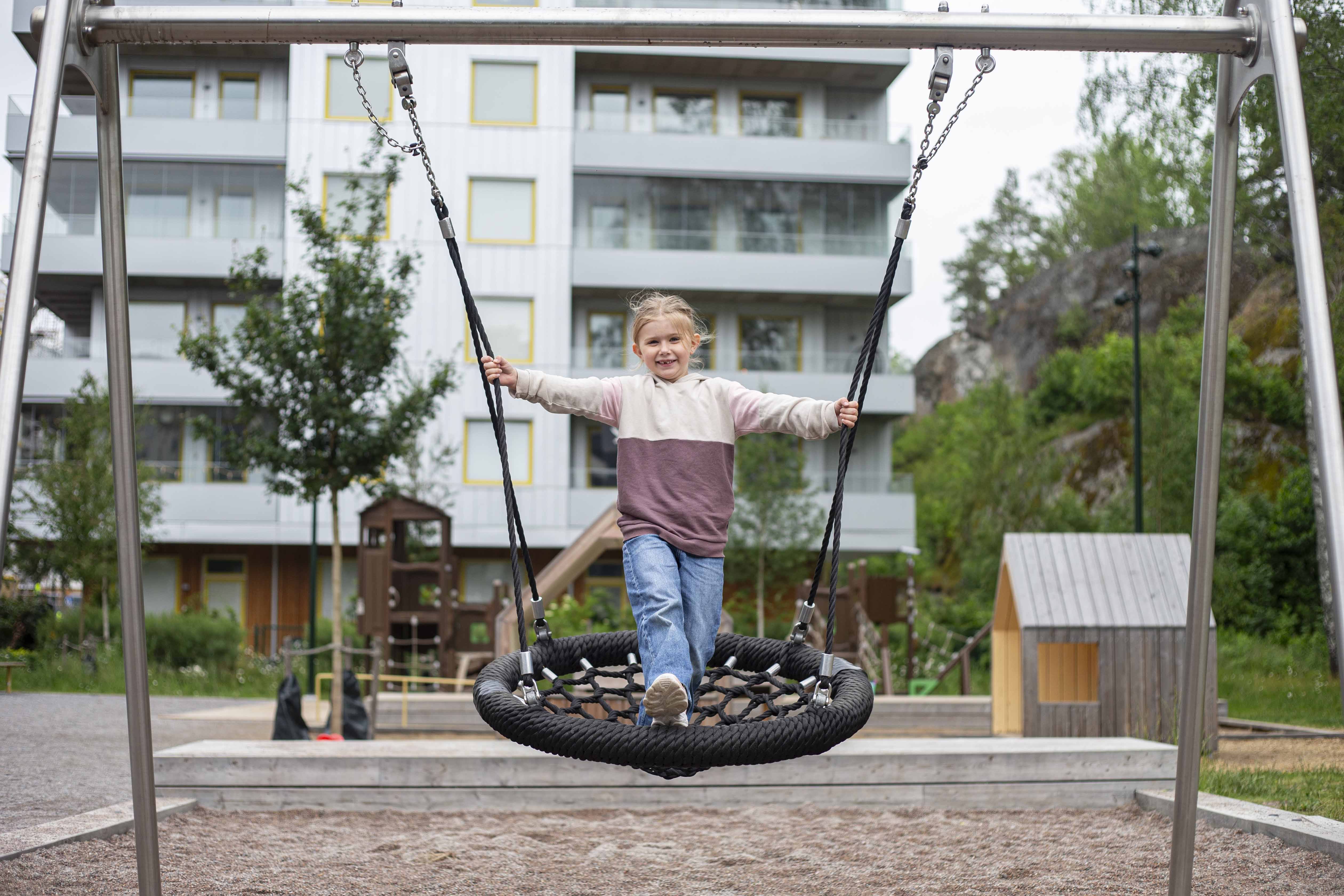 Flicka som gungar i en lekpark i Vega med hus i bakgrunden