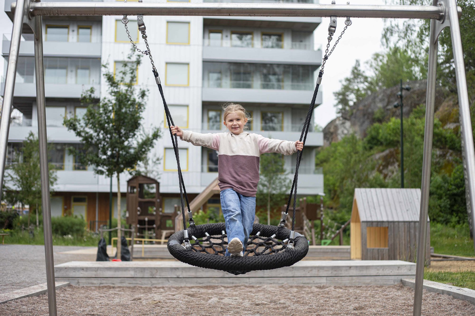 Flicka som gungar i en lekpark i Vega med hus i bakgrunden