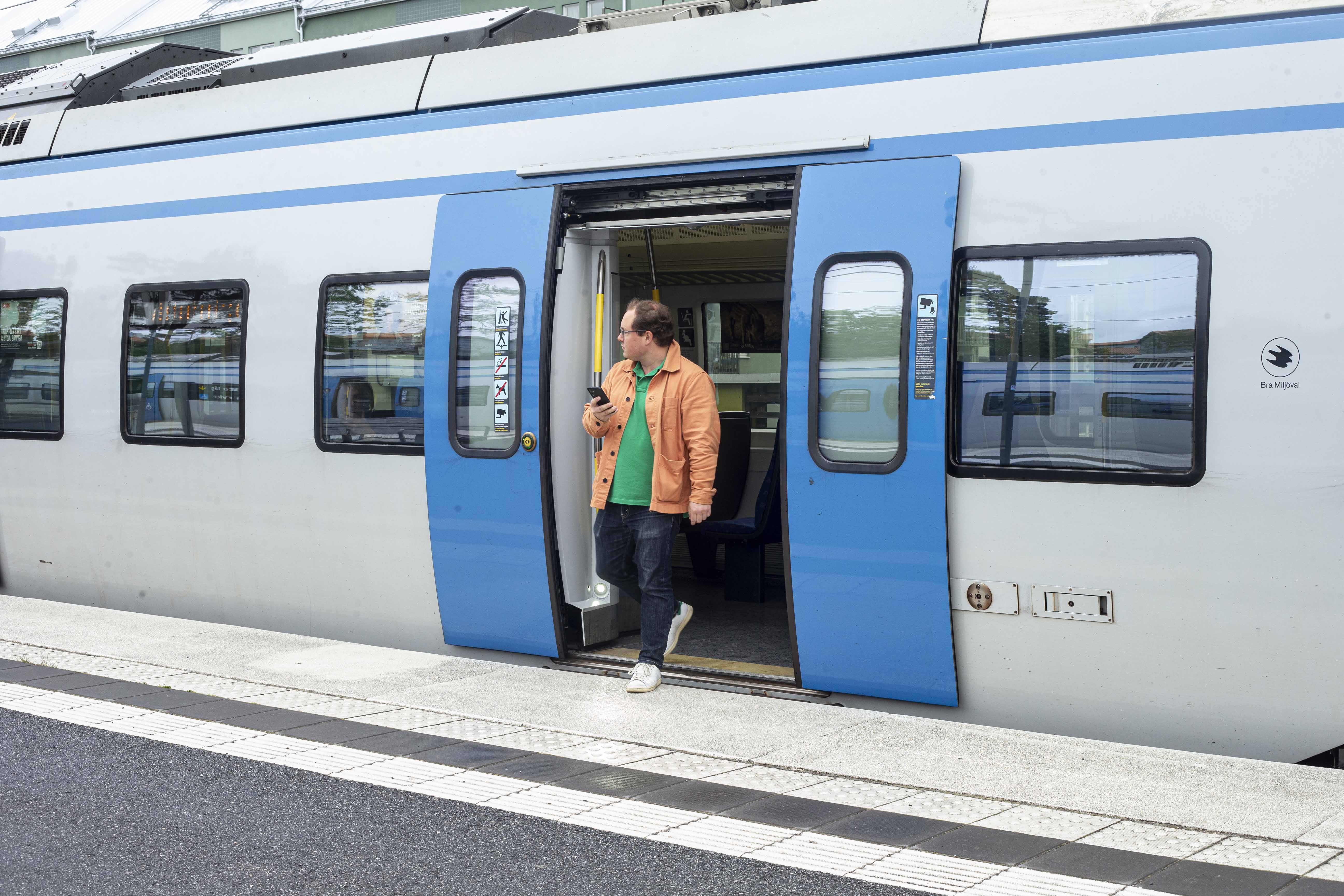 Man i orange jacka går av pendeln och håller i telefonen